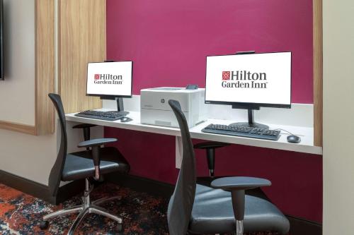 two computer monitors sitting on a desk with chairs at Hilton Garden Inn Longmont in Longmont