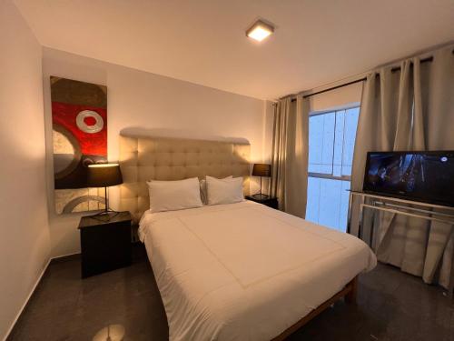 1 dormitorio con 1 cama blanca y TV en Apartamento en Miraflores La paz, en Lima