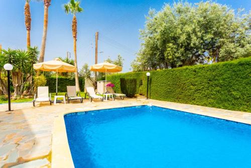 a swimming pool with chairs and umbrellas in a yard at Villa Halima Alexandros in Polis Chrysochous
