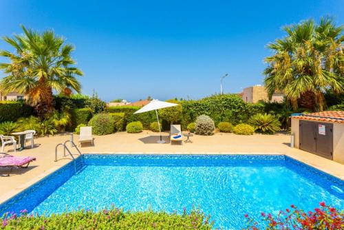 a swimming pool with chairs and an umbrella and palm trees at Villa Fortuna in Polis Chrysochous