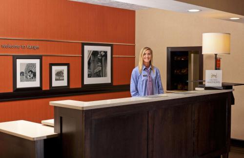 a woman standing behind a counter in a waiting room at Hampton Inn & Suites Fargo Medical Center in Fargo