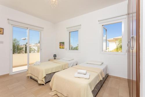 Duas camas num quarto branco com janelas em Villa Miranda em Paralimni