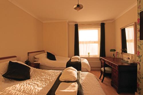um quarto com 2 camas, uma secretária e uma janela em The Crow's Nest em Broadstairs