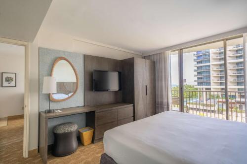 a bedroom with a bed and a tv and a window at Embassy Suites by Hilton Waikiki Beach Walk in Honolulu