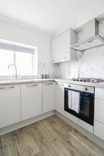 a white kitchen with white cabinets and a sink at Modern House with Gated Driveway and Free WiFi in Luton