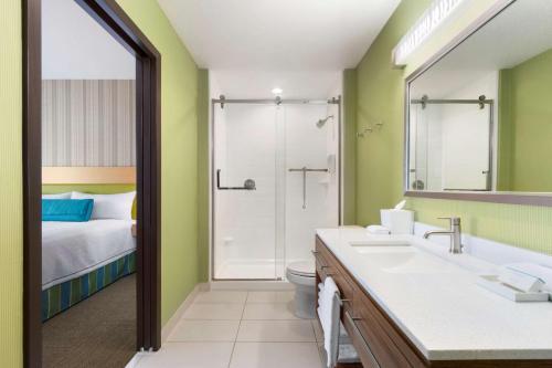 a bathroom with a sink and a shower and a bed at Home2 Suites by Hilton Houston Stafford - Sugar Land in Stafford