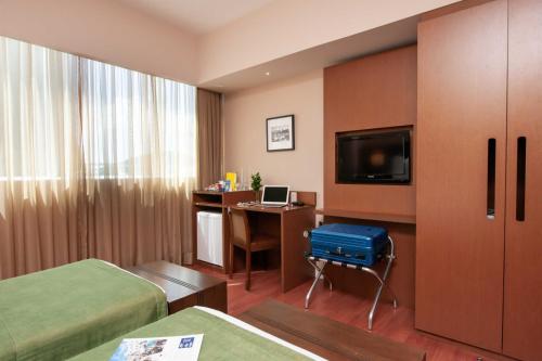 a hotel room with two beds and a desk and a tv at Golden Tulip Porto Vitória in Vitória