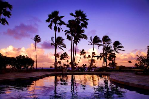 a pool with palm trees in front of a sunset at Hilton Garden Inn Kauai Wailua Bay, HI in Kapaa