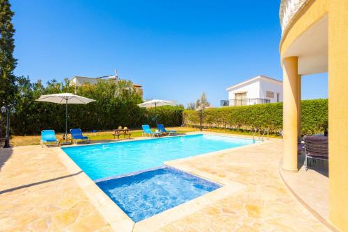 a swimming pool with chairs and umbrellas next to a house at Villa Tsikkos Tessera in Argaka