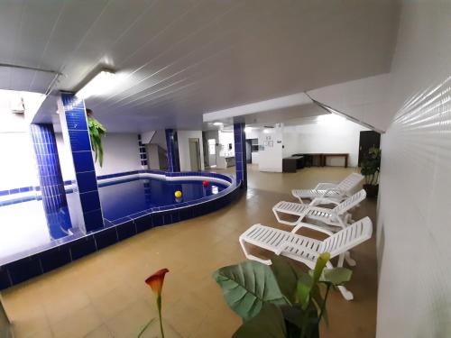 Hotel Plaza Center في سانتا كروز دي لا سيرا: حمام سباحة داخلي كبير مع كراسي بيضاء في مبنى