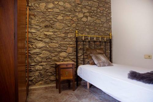 1 dormitorio con pared de piedra, cama y mesa en Casa Jarca 1er piso, a 1km de Canillo, en Canillo
