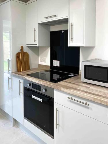 a kitchen with white cabinets and a black oven and microwave at Modern flat near train station with free parking in Cambridge