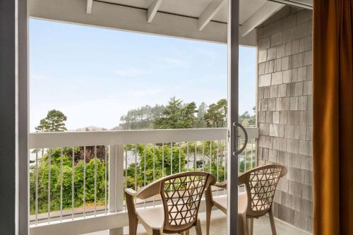 a room with a balcony with two chairs and a window at Travelodge by Wyndham Depoe Bay in Depoe Bay