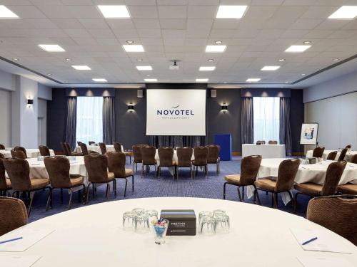 a conference room with a table and chairs and a screen at Novotel London Stansted Airport in Stansted Mountfitchet