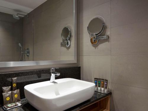 ein Badezimmer mit einem weißen Waschbecken und einem Spiegel in der Unterkunft Novotel London Stansted Airport in Stansted Mountfitchet