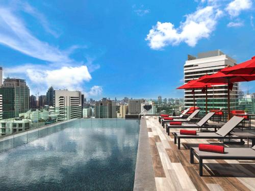 a swimming pool with lounge chairs and a city skyline at Novotel Bangkok Sukhumvit 4 in Bangkok