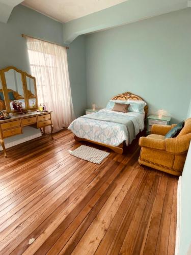 een slaapkamer met een bed en een stoel en houten vloeren bij espectacular departamento centro de quito in Quito