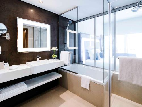a bathroom with two sinks and a glass shower at Novotel Fujairah in Fujairah