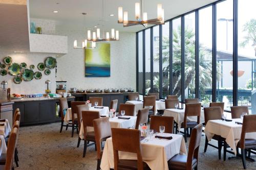 un restaurante con mesas y sillas blancas y ventanas en Hilton Galveston Island Resort, en Galveston