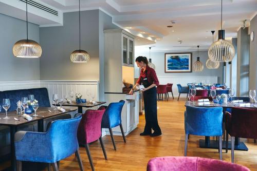 a woman standing in a restaurant with tables and chairs at Dorint Strandresort & Spa Ostseebad Wustrow in Wustrow