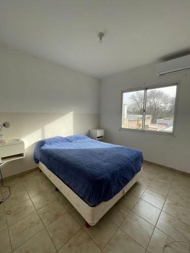 a bedroom with a bed with a blue comforter and a window at DUPLEX BV in Bell Ville