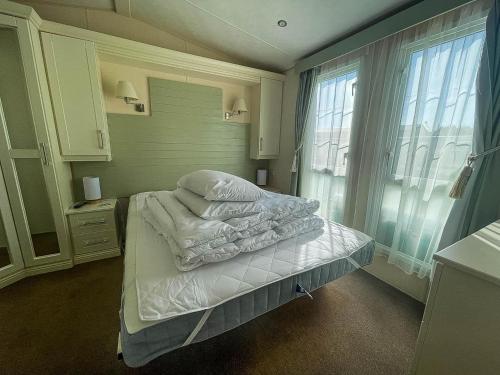 a bedroom with a bed with white sheets and a window at Lovely Caravan With Decking At Manor Park, Near Hunstanton Beach Ref 23034c in Hunstanton