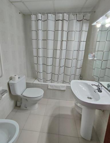 a white bathroom with a toilet and a sink at Hotel Cogullada in Zaragoza
