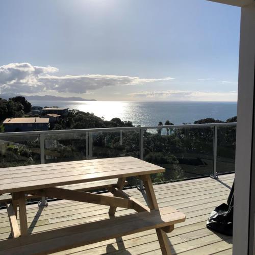 - une table de pique-nique en bois sur une terrasse avec vue sur l'océan dans l'établissement Hosts on the Coast Sea Blue Hideaway, à Kuaotunu