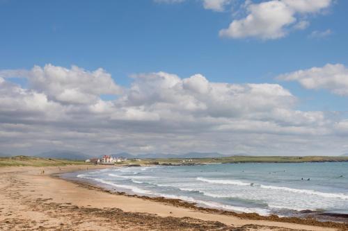 a beach with people swimming in the ocean at Crows Nest - Rhosneigr in Rhosneigr