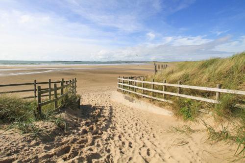 a sandy beach with a wooden fence and a wooden at Crows Nest - Rhosneigr in Rhosneigr