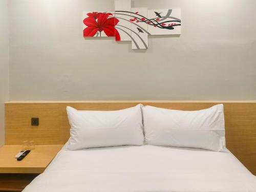 un letto con lenzuola bianche e un fiore rosso su una parete di Travel Biz Hotel Medan Mitra RedDoorz a Medan