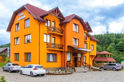 un bâtiment orange avec des voitures garées devant lui dans l'établissement У Румуна, à Yasinya