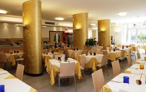 a restaurant with white tables and chairs and gold columns at Eraclea Palace Hotel 4 stelle S in Eraclea Mare