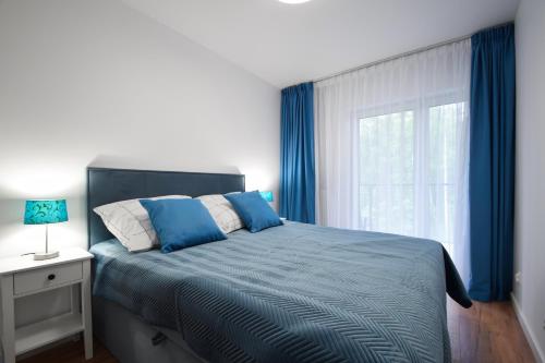 a bedroom with a bed with blue curtains and a window at Apartamenty Międzywodzie Plażowa Park in Międzywodzie