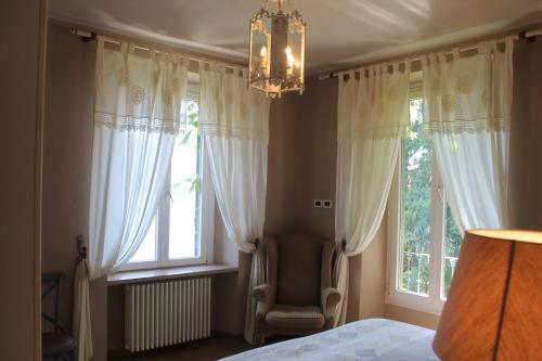 a bedroom with a chandelier and two windows at VILLA SASSO Depandance in Cannobio