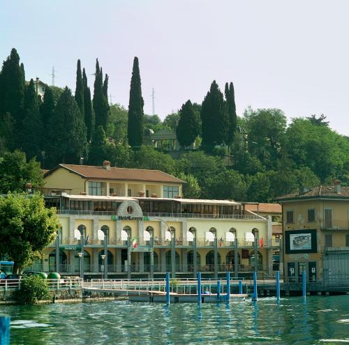a building on the water with trees in the background at Hotel Lovere Resort & Spa in Lovere