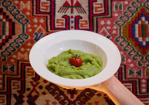 a person holding a bowl of green sauce with a tomato in it at Toon Armeni Guest House in Dilijan