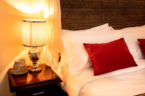 a bed with a red pillow and a lamp on a table at Club Mango Resort in Kalpitiya