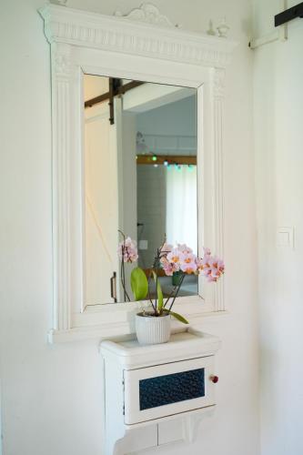 a white bathroom with a mirror and flowers on a counter at matyóróza vendégház in Tard