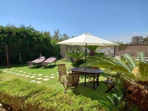 a patio with a table and chairs and an umbrella at Green Rooms - Casa nel verde in Pachino