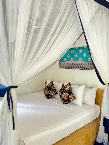 a bed with white curtains and pillows on it at Karanga Bungalows in Michamvi