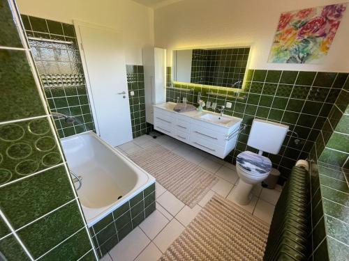 baño de azulejos verdes con bañera y aseo en Fewo Zum Wohlfühlen, en Hemmoor