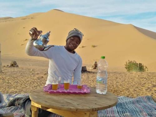 Un uomo seduto nel deserto con un tavolo con bevande di Gambe Camp ad Adrouine