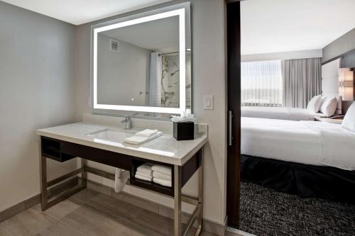 a bathroom with a sink and a bed and a mirror at Embassy Suites By Hilton Oklahoma City Northwest in Oklahoma City