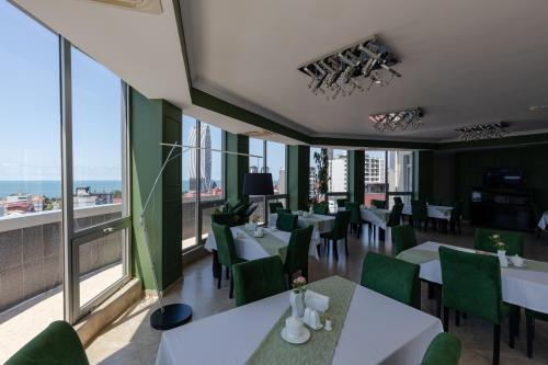 un restaurante con mesas blancas, sillas verdes y ventanas en Hotel Aisi, en Batumi