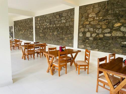 a restaurant with wooden tables and chairs and a stone wall at Thiksay Organic Resort in Ranbirpura