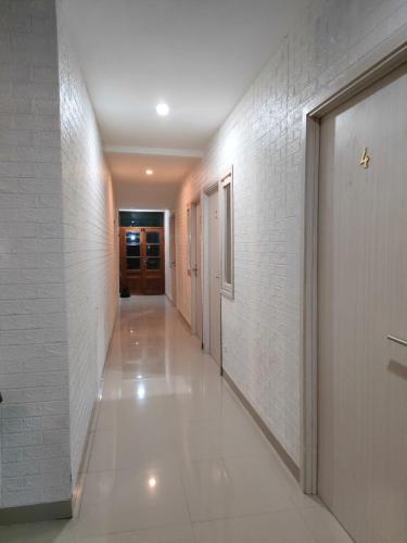 a long hallway with white tile walls and a door at Cahaya Losmen Sragen in Sragen