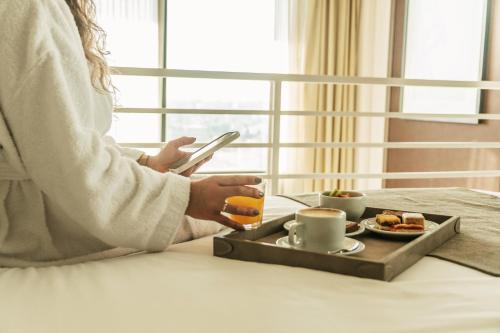 a woman sitting at a table with a tray of food and a cell phone at Mulen Hotel Tandil in Tandil