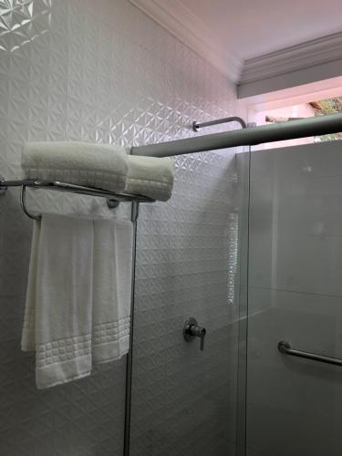 una ducha con toallas blancas y una puerta de ducha de cristal en Villa Hotel, en Rio Piracicaba