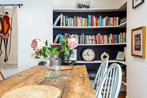 uma mesa de jantar com um vaso de flores e livros em Cottage Style Three Bedroom House em Londres